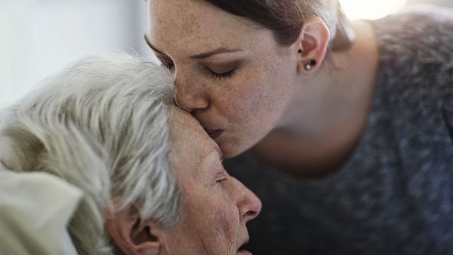 Una mujer joven besa en la frente a una anciana acostada