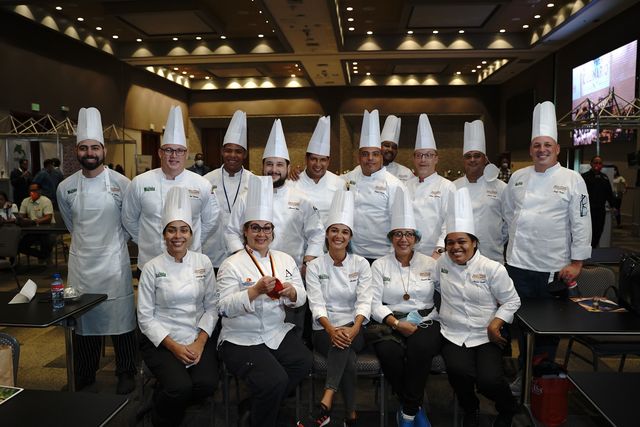 Un grupo de chefs con filipinas blancas posa en un salón de eventos