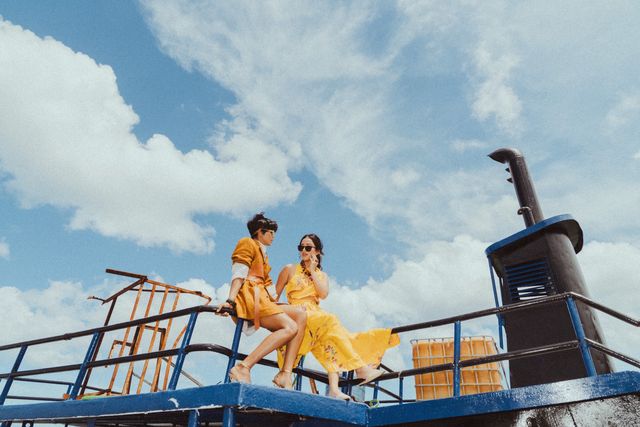 Dos modelos vestidas de amarillo sentadas en la cubierta de un barco bajo el cielo azul