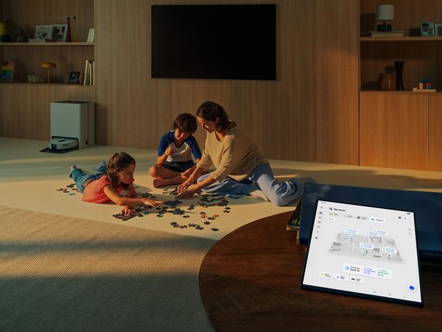 Una familia juega en la sala mientras una tableta muestra el panel de control del hogar conectado