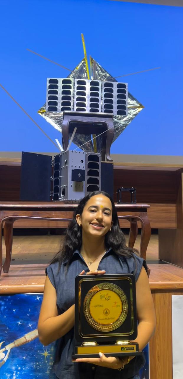 Annette Vásquez sostiene un reconocimiento junto a una maqueta de satélite