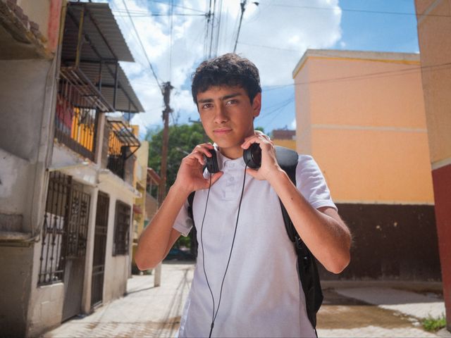 008RACCA con audífonos al cuello y mochila en una calle de su barrio