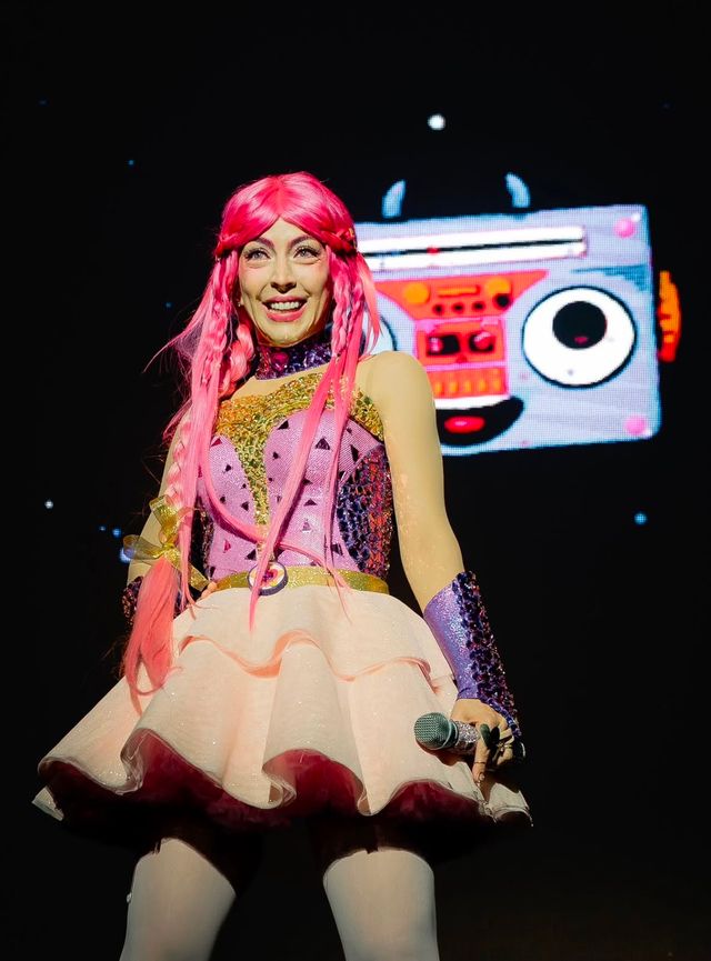 Luli Pampín en el escenario con vestido de colores y un personaje en forma de radio