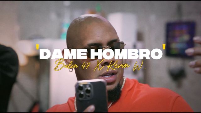 Bulin 47, con gafas de sol y camiseta roja, en una escena del video oficial de «Dame hombro»