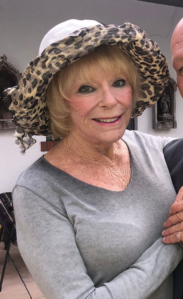 Elke Sommer sonríe con un sombrero de estampado de leopardo y suéter gris