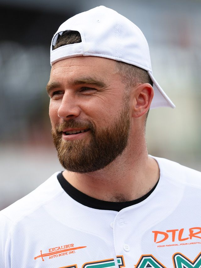 Travis Kelce sonríe con una gorra blanca puesta al revés en un juego benéfico de sóftbol