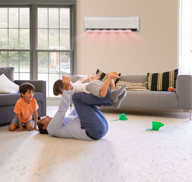 Un padre juega con sus hijos en la sala bajo un aire acondicionado Samsung