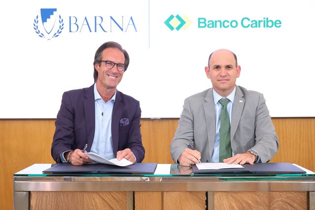 Paulo Alves y Edgar Del Toro firman el acuerdo frente a los logos de BARNA y Banco Caribe