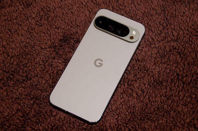 Un teléfono Google Pixel 9 Pro XL de color claro, visto por detrás, sobre una manta marrón