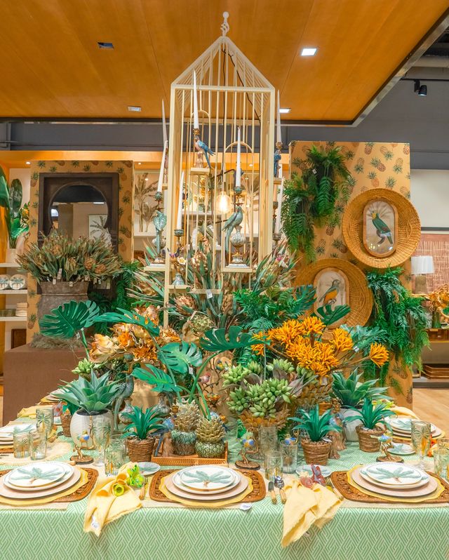 Mesa montada con vajilla, plantas tropicales y una jaula decorativa