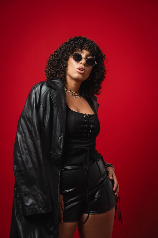Ivy Negro posa de cuerpo entero con abrigo de cuero frente a un fondo rojo