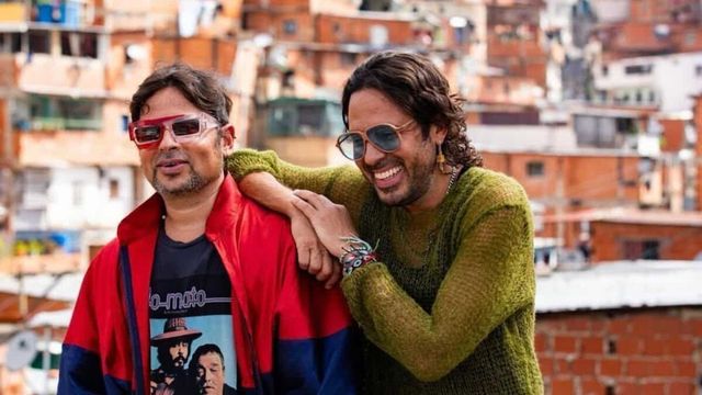 Servando y Florentino abrazados frente a un barrio de casas de ladrillo