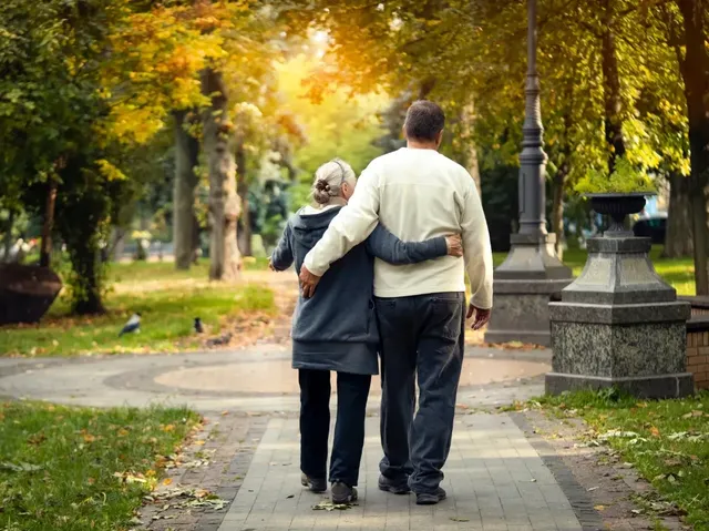 Una pareja mayor camina abrazada por un parque
