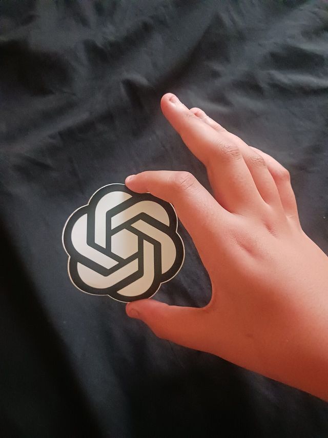 Una mano sostiene una calcomanía con el logotipo de OpenAI