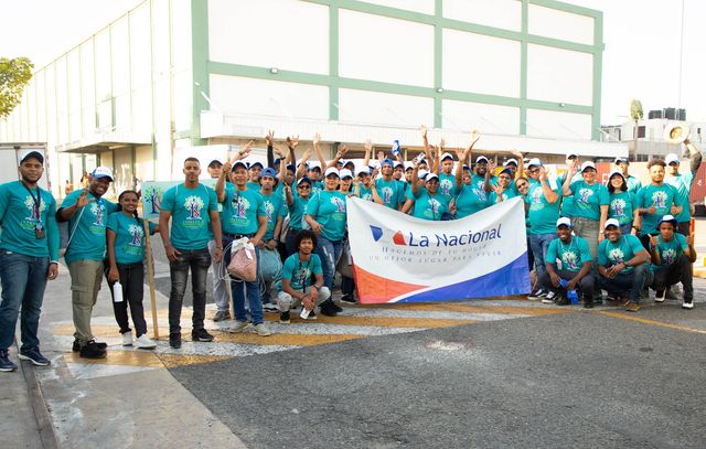 Voluntarios de La Nacional con camisetas verdes posan con la bandera de la empresa antes de la jornada